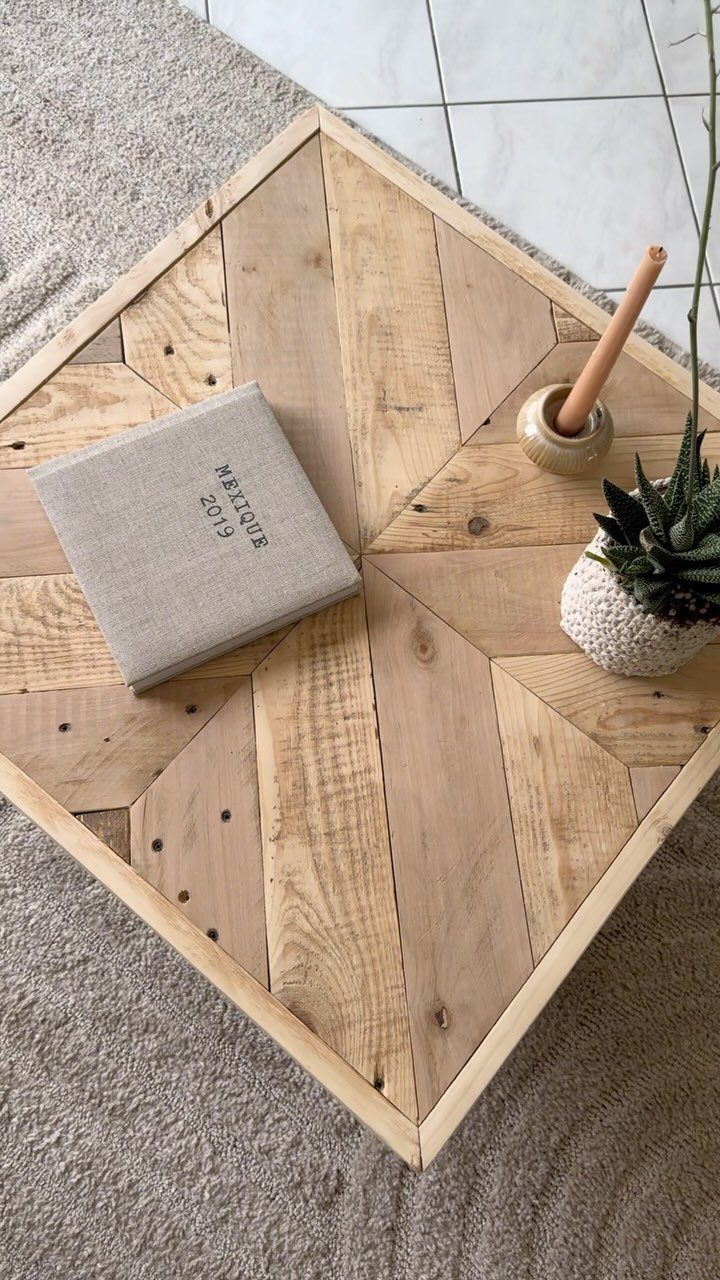 Pallet wood coffee table with a geometric plank top, notebook, and small plant.