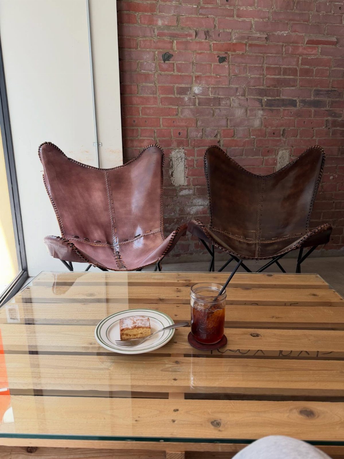 Pallet wood coffee table with glass top, cake, and coffee before leather chairs.