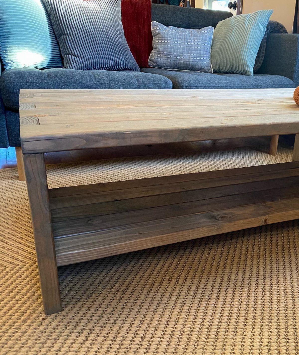 Pallet wood coffee table with a lower shelf on a woven tan rug.