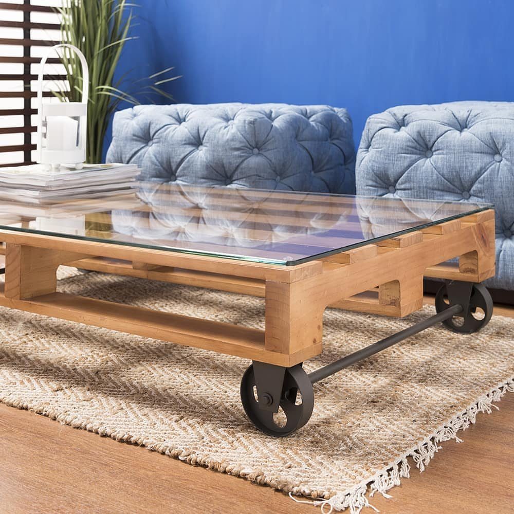 Pallet wood coffee table with glass top and black metal wheels on jute rug