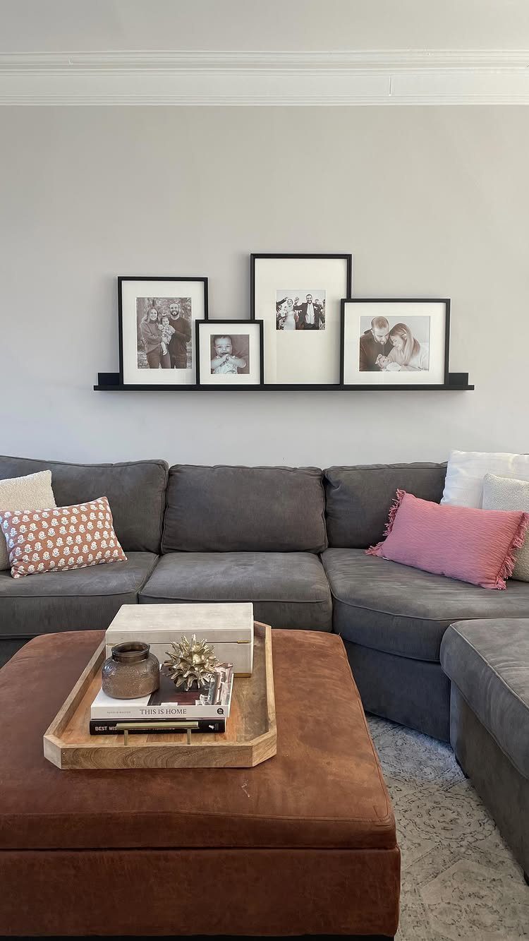 Black picture ledge with framed photos mounted on a wall above a grey sofa.