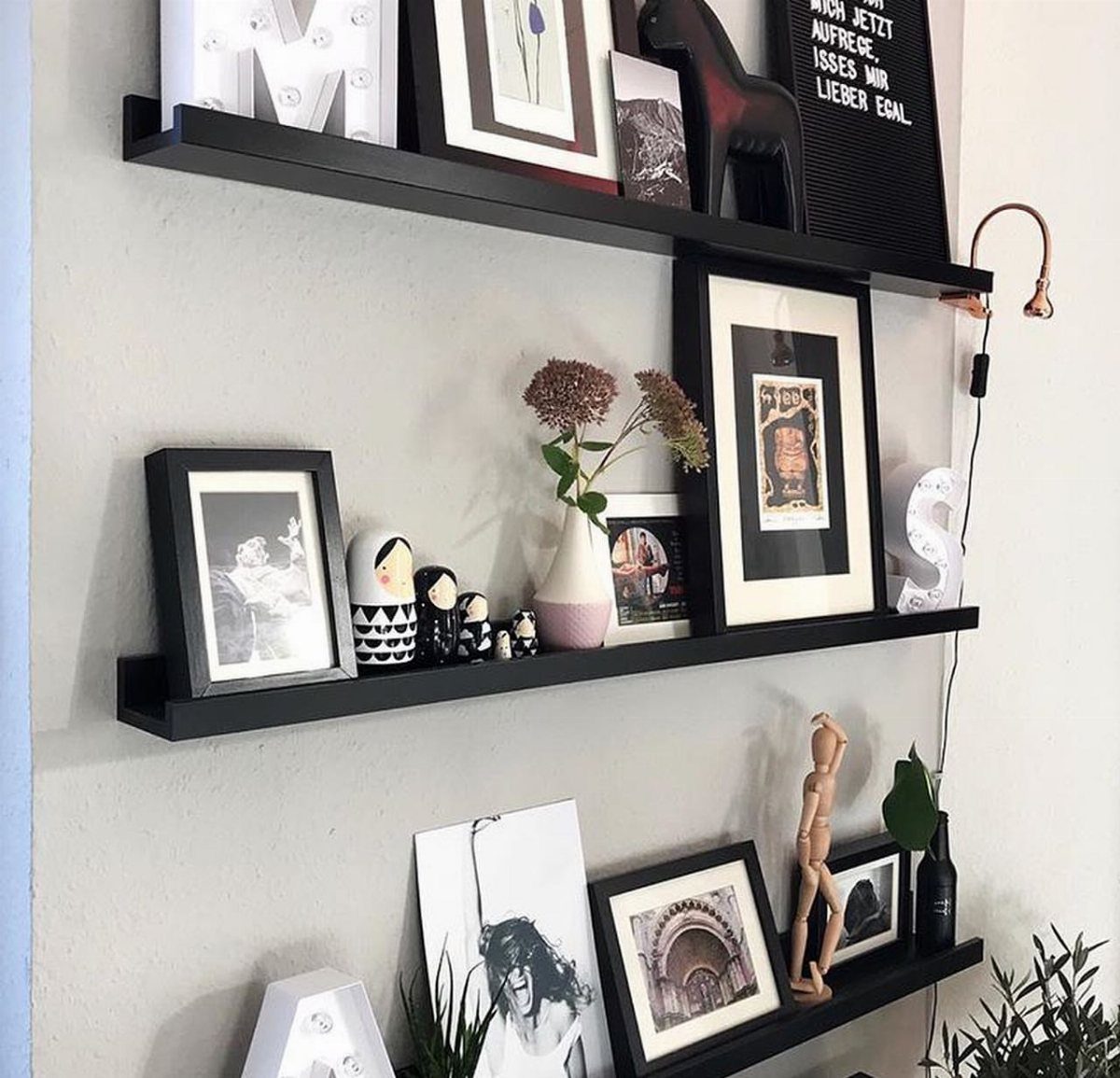 Black floating picture ledges displaying framed art, figurines, and decor on a white wall.
