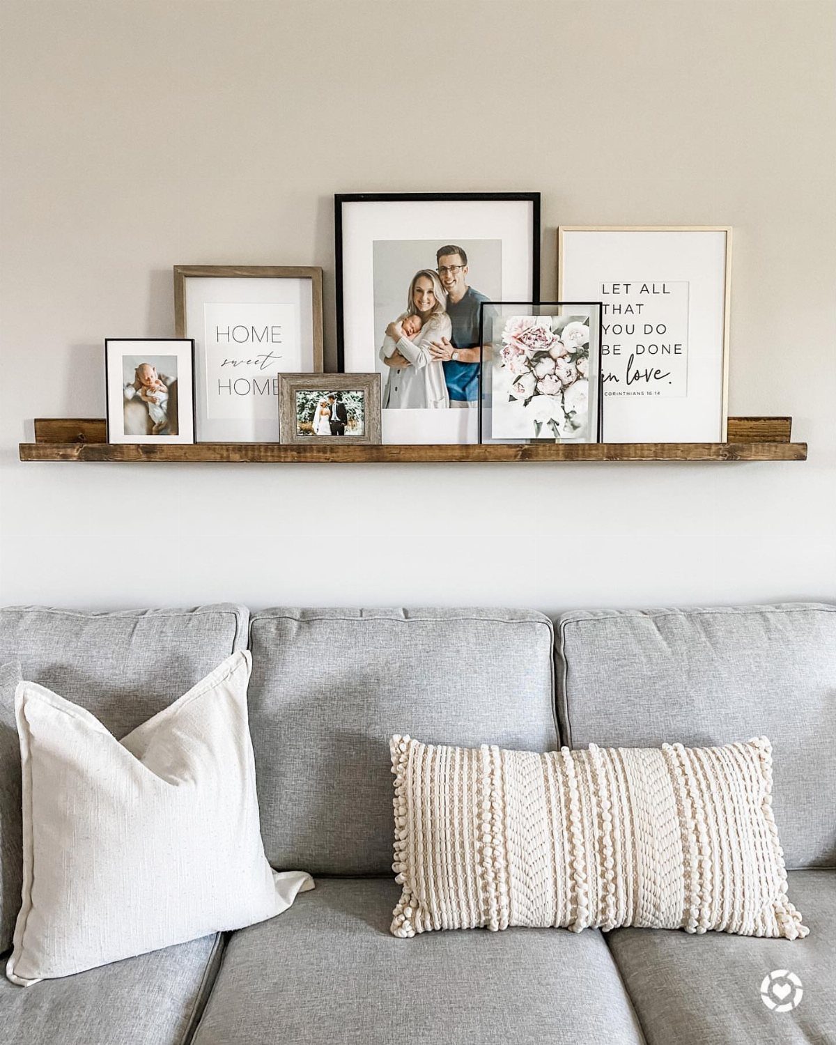 Wooden picture ledge above a grey couch featuring a variety of framed art pieces.