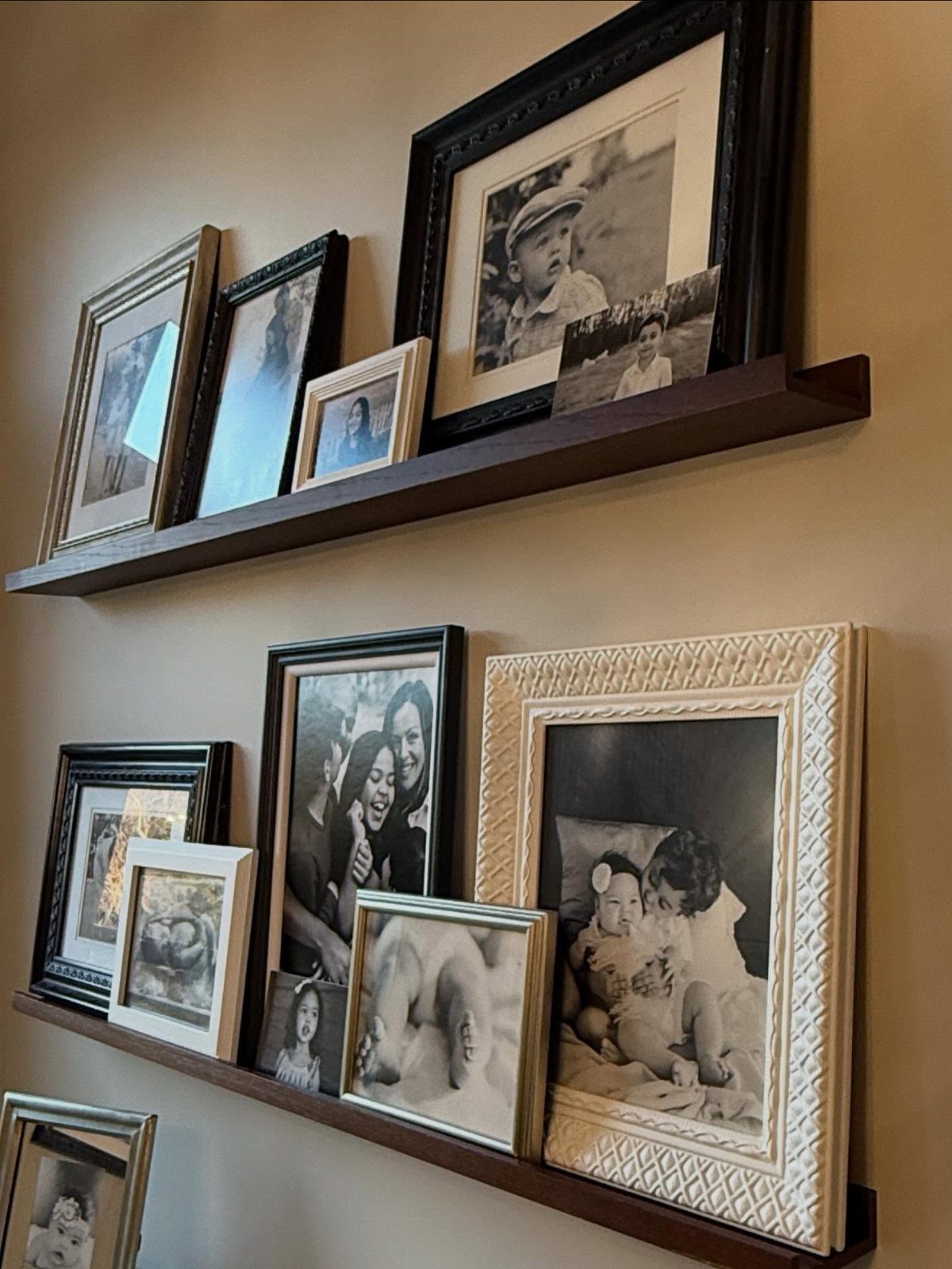 Framed black and white photographs resting on two dark brown floating wall shelves.