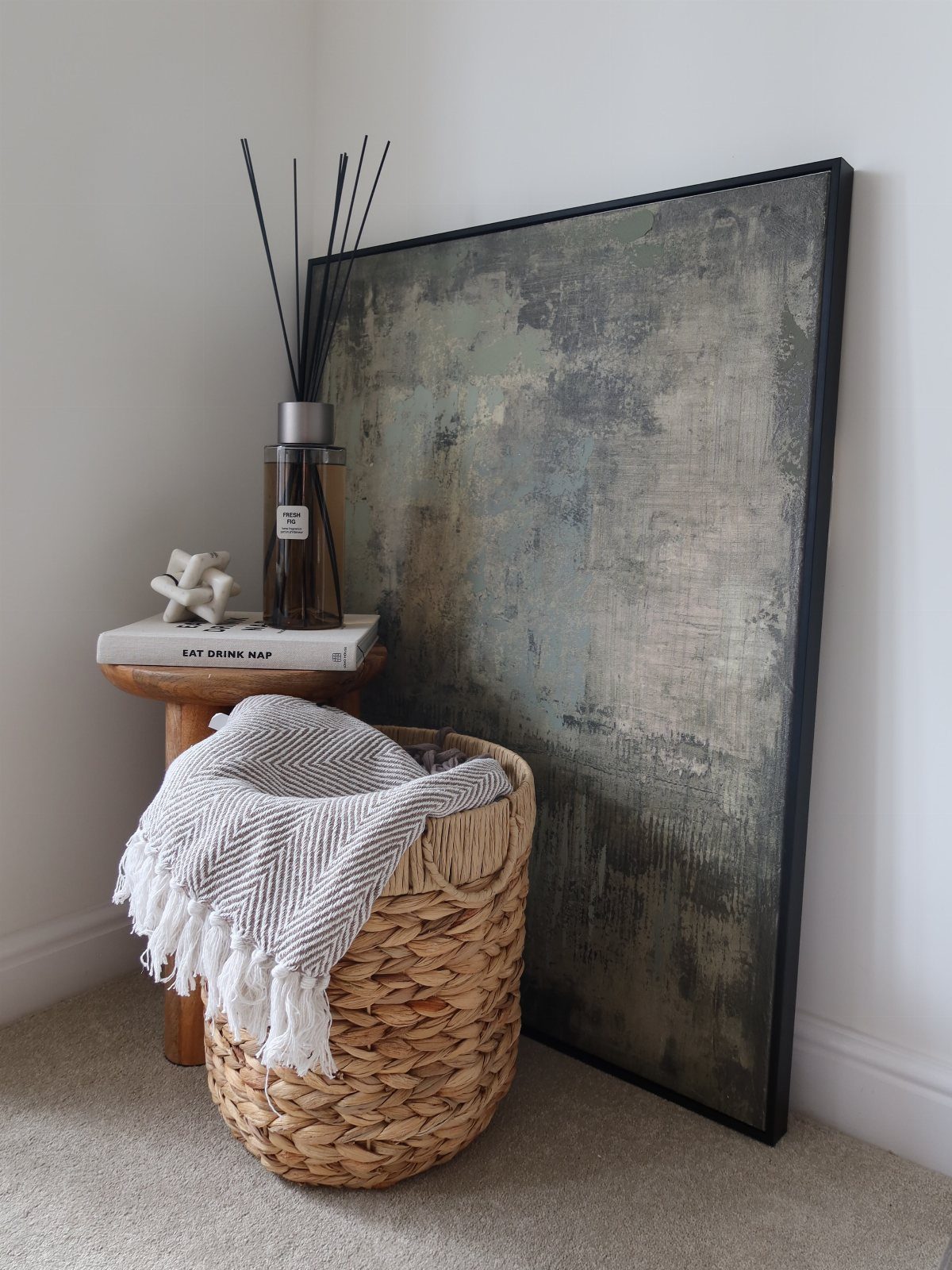 Large abstract painting leaning against a white wall next to a woven basket.