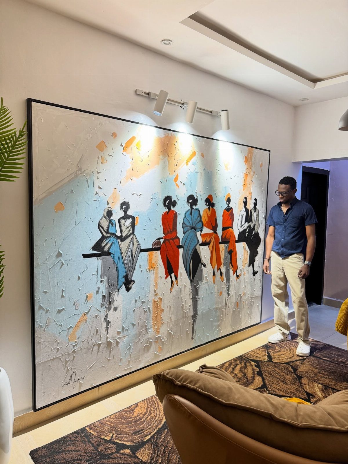 Large rectangular painting of stylized figures hanging on a white living room wall.