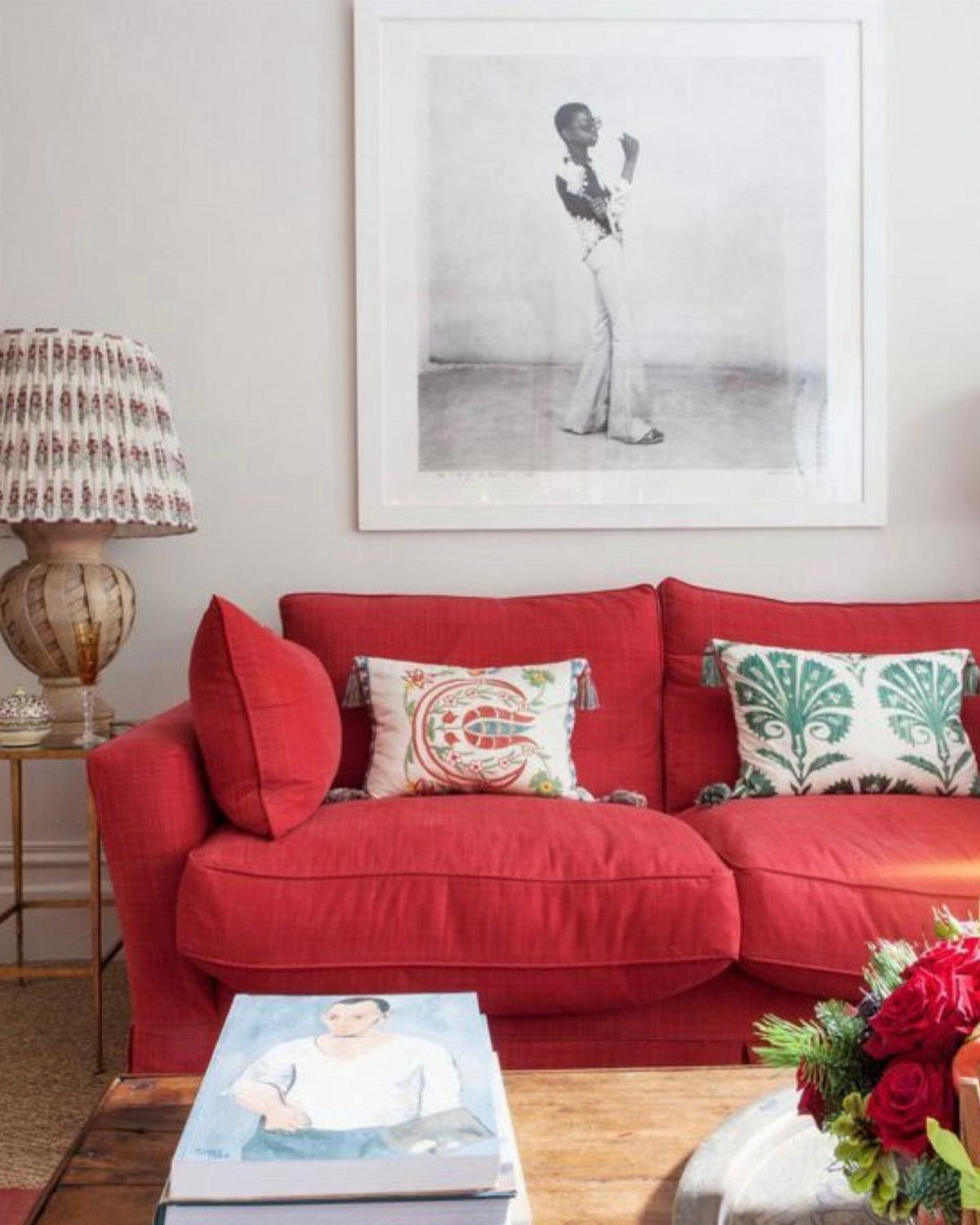 Red fabric sofa with patterned pillows and a black and white portrait above.