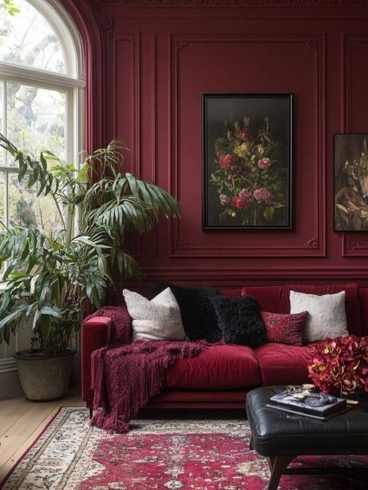 Red velvet couch in a living room with matching red paneled walls and plants.
