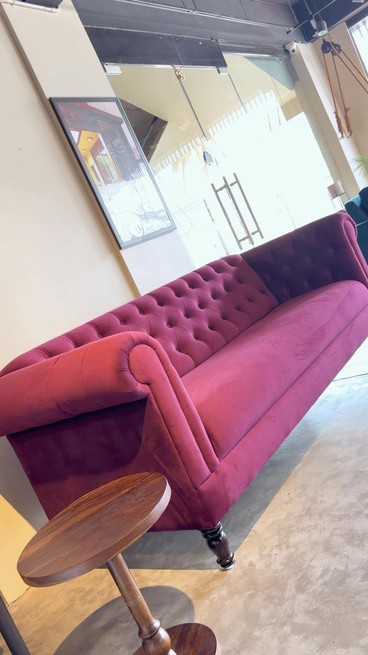 Deep red velvet tufted chesterfield sofa with a small wooden side table nearby.
