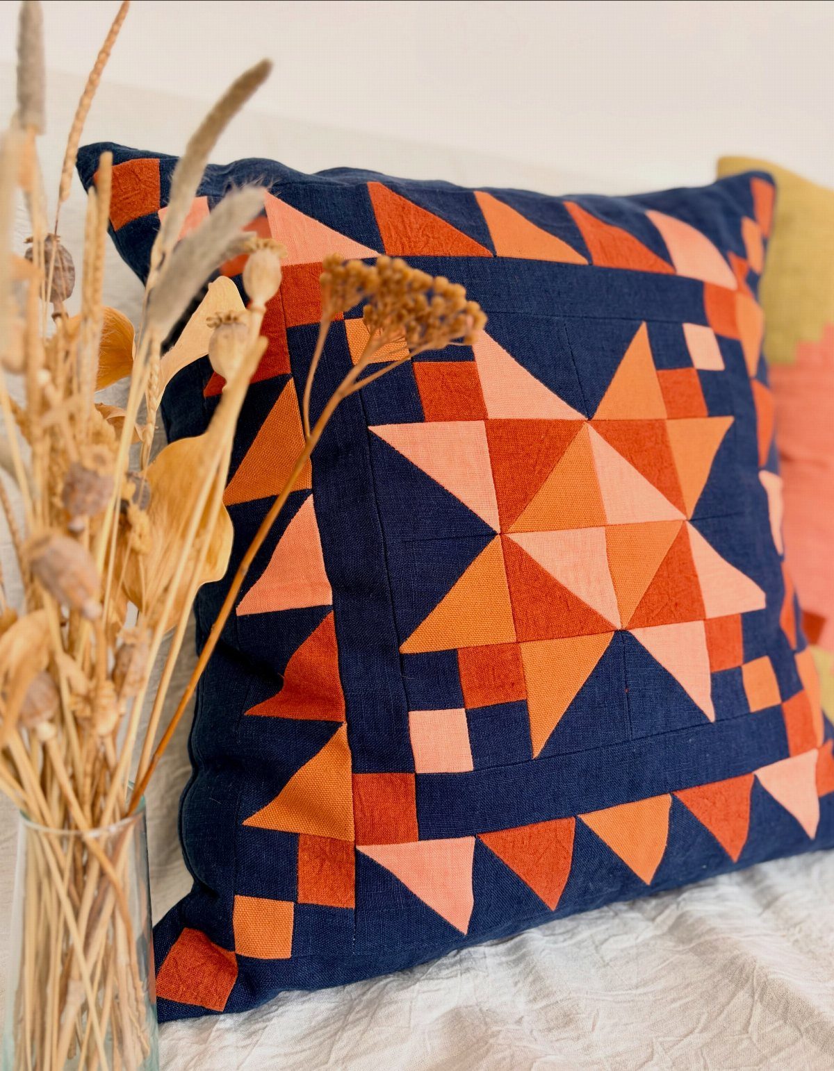 Star-patterned navy and orange quilt pillow resting on a white fabric surface.