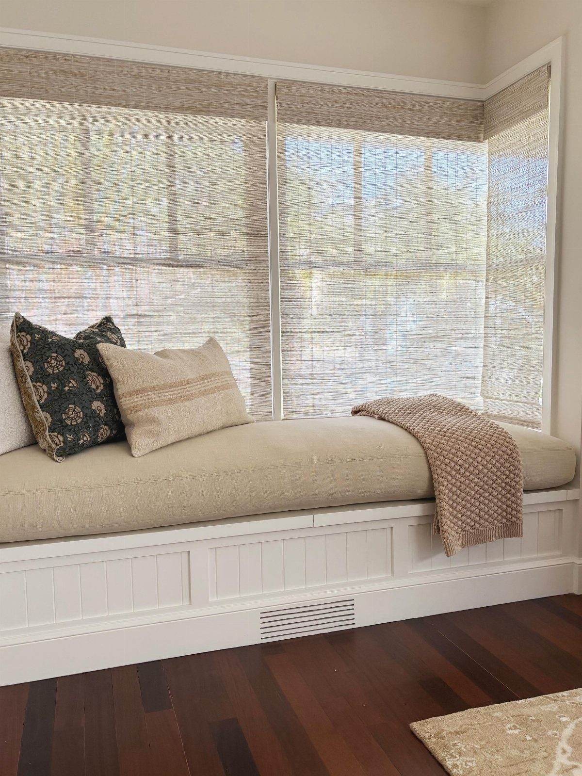 Woven bamboo blinds covering a window above a cozy built-in window seat.