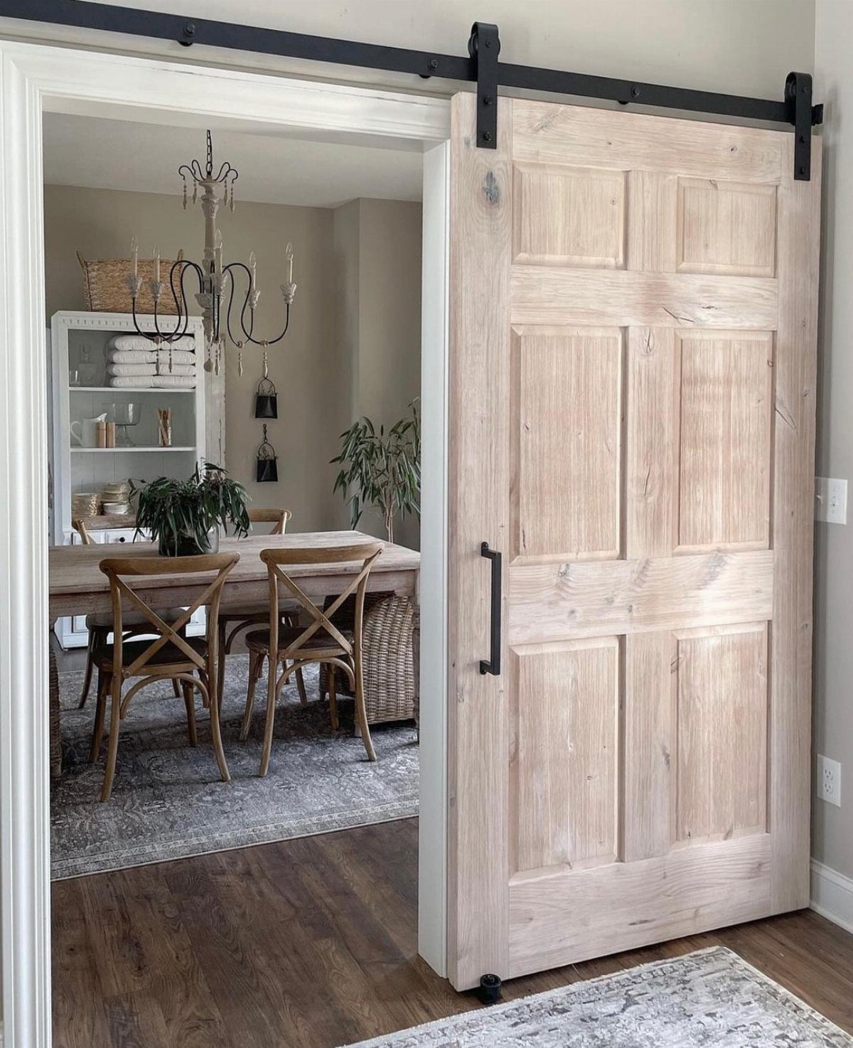 Light wood sliding barn door with black hardware opening into a dining room.