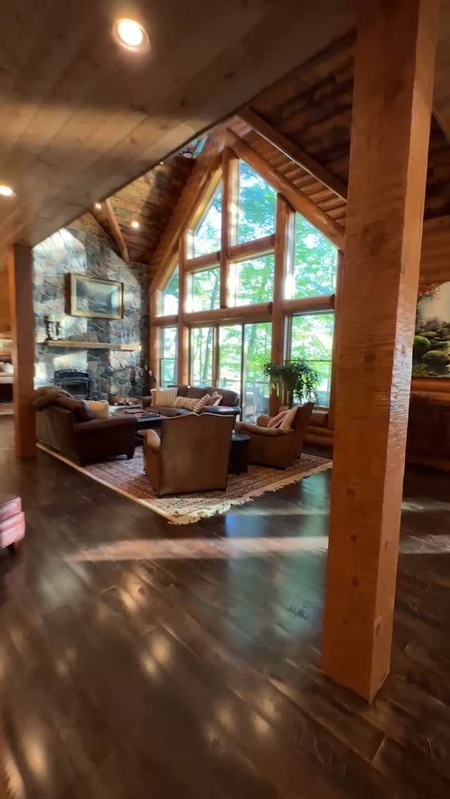 Stone fireplace in a rustic living room with vaulted ceilings and large windows.