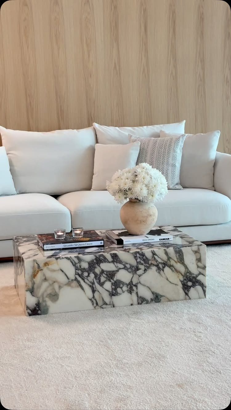 Marble coffee table with books and flowers in front of a white sectional sofa