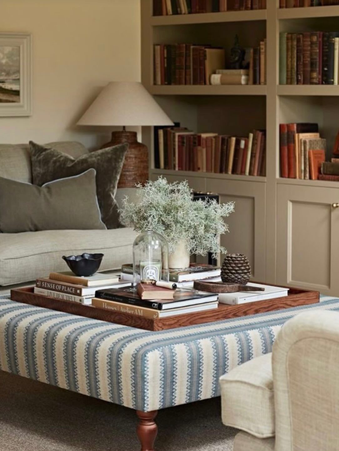 Striped upholstered ottoman coffee table with a wooden tray and books in a living room