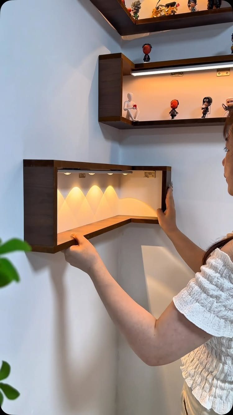 Woman adjusting a brown wooden L-shaped floating wall shelf with integrated LED lighting.