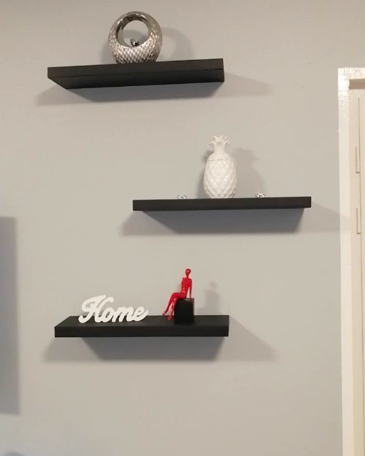Three black floating shelves on a grey wall with decorative home ornaments.