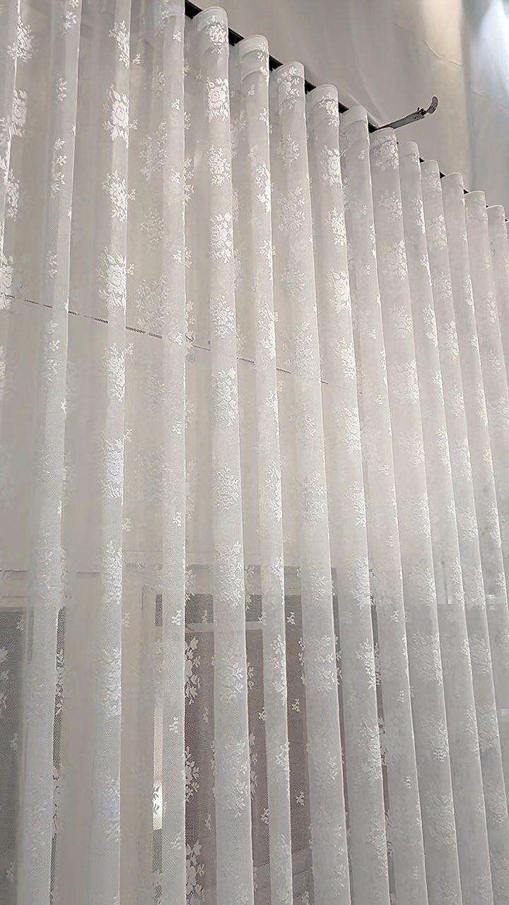 White sheer curtains with floral patterns hanging from a dark curtain rod.