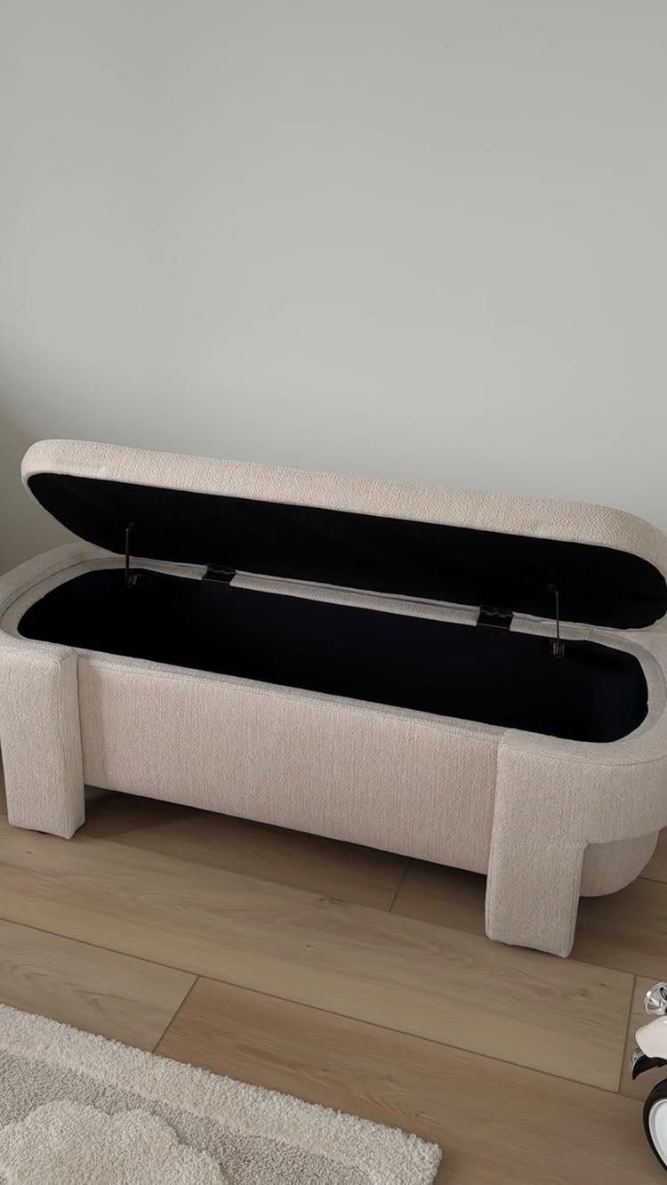 Beige fabric storage ottoman with open lid on a light wood floor