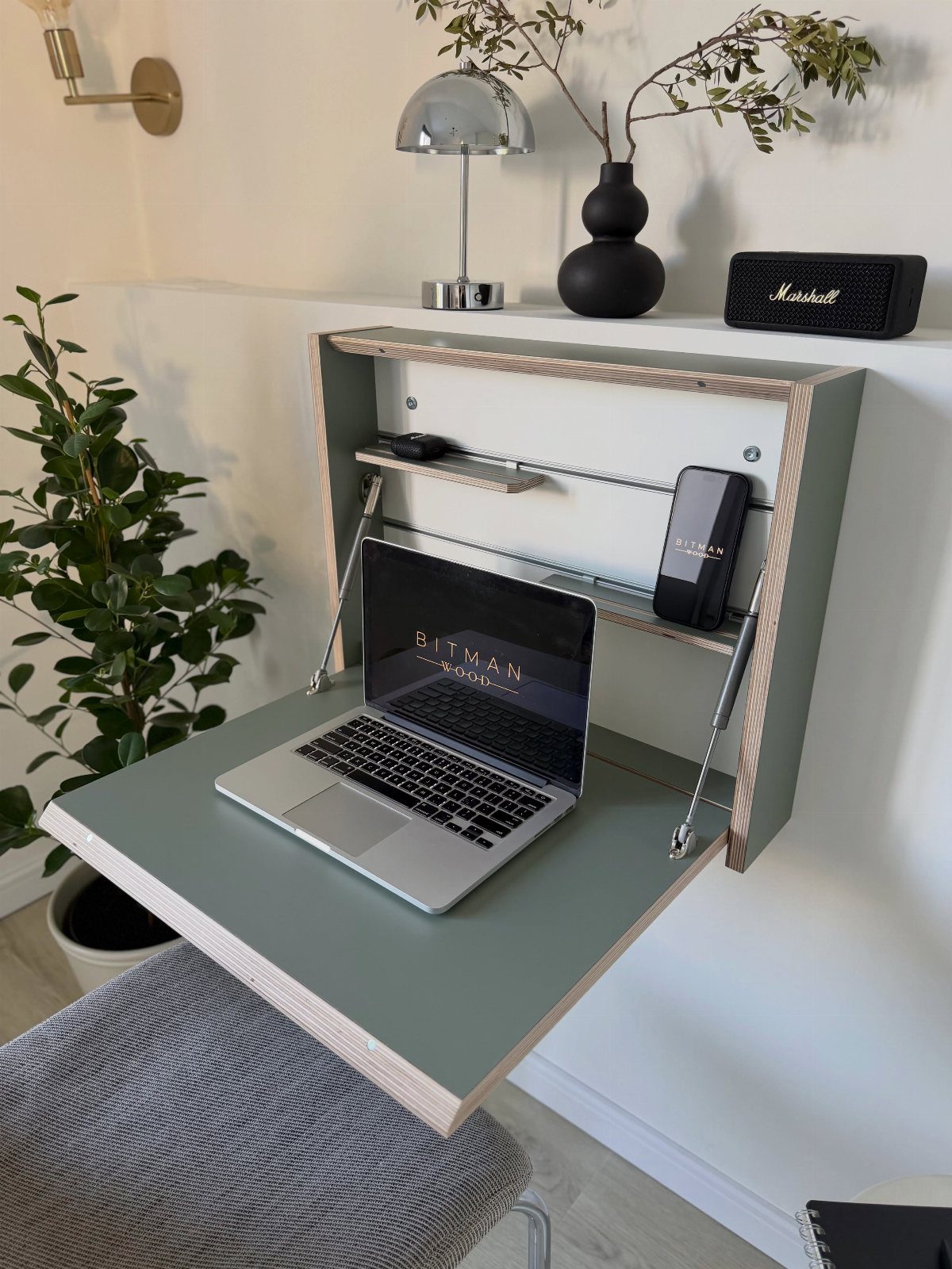 Wall-mounted folding sage green desk with a laptop and small storage shelves.