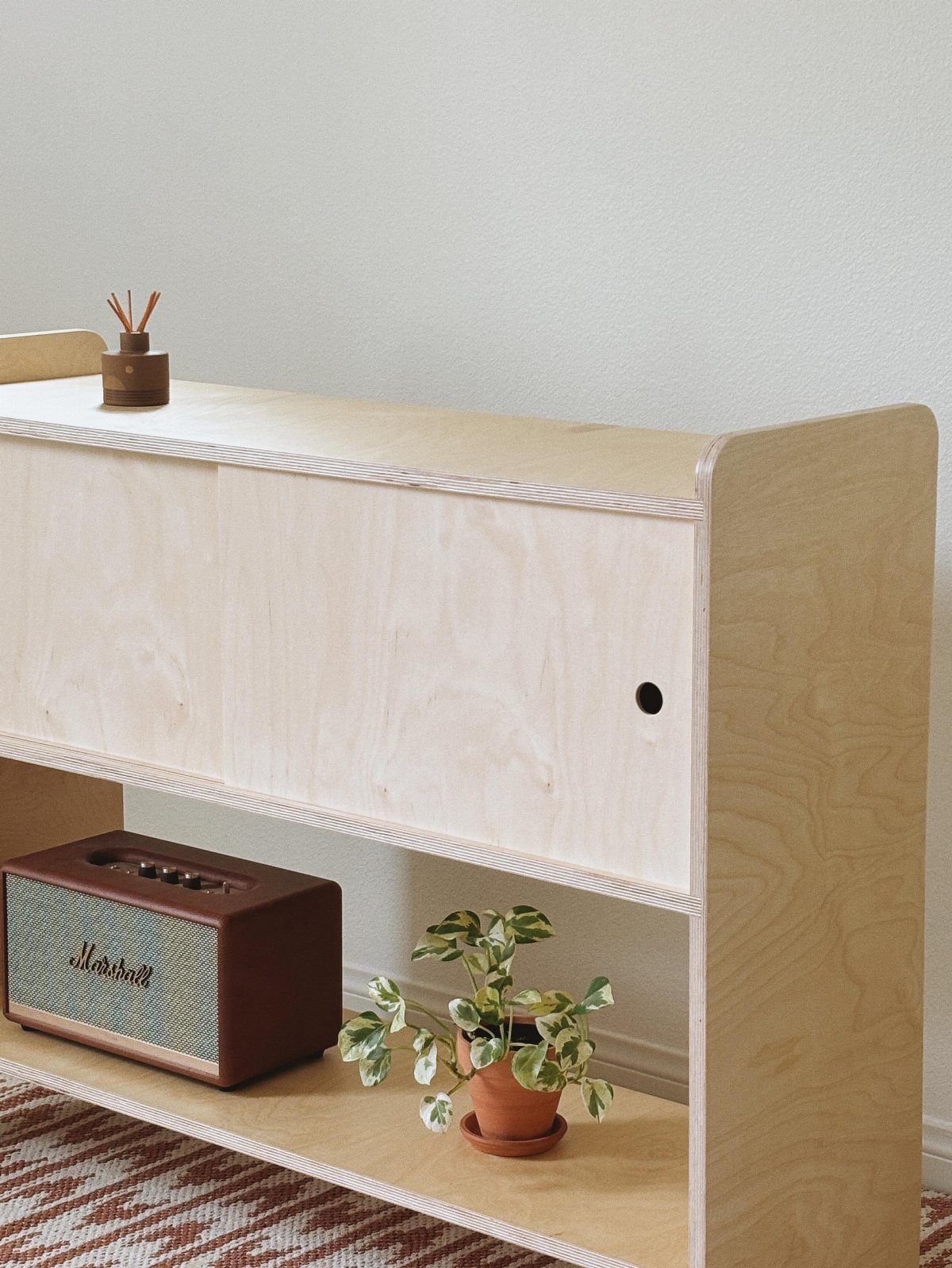Plywood sideboard with a Marshall speaker and a small potted plant on a shelf.