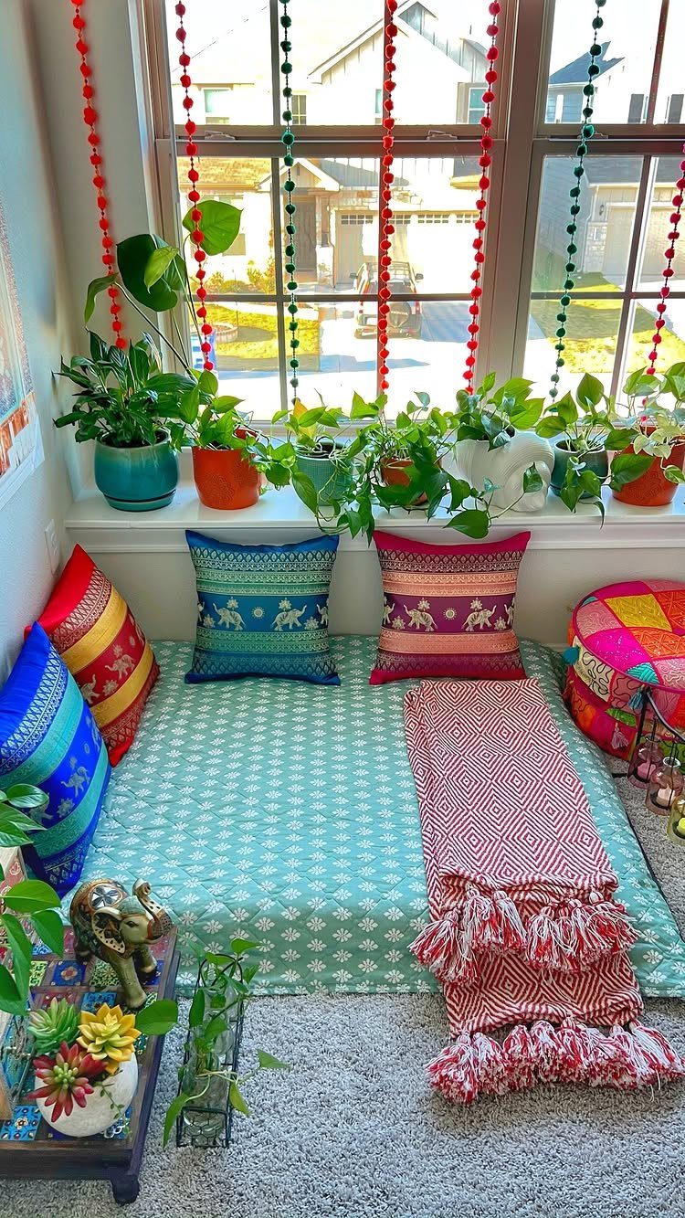 Cozy window seat with turquoise floor cushion, colorful pillows, and potted plants.