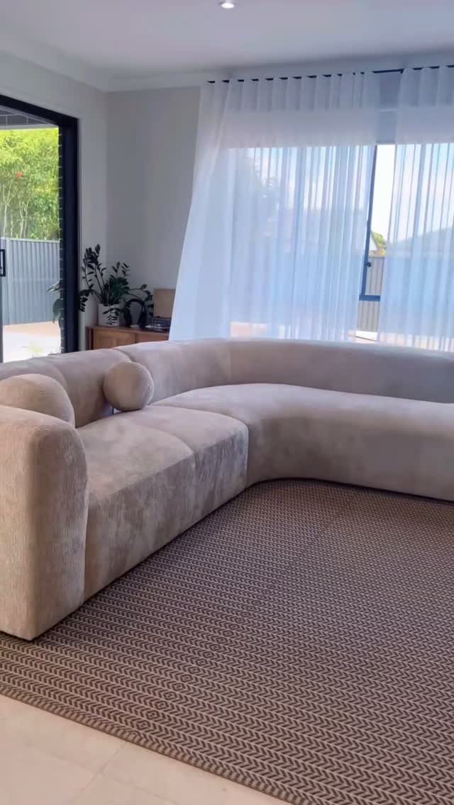 Beige curved sectional sofa on a brown textured rug in a bright living room.