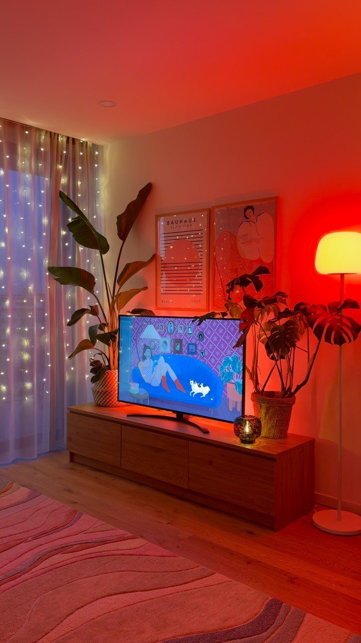 Living room with a red floor lamp, fairy lights, and a television console.