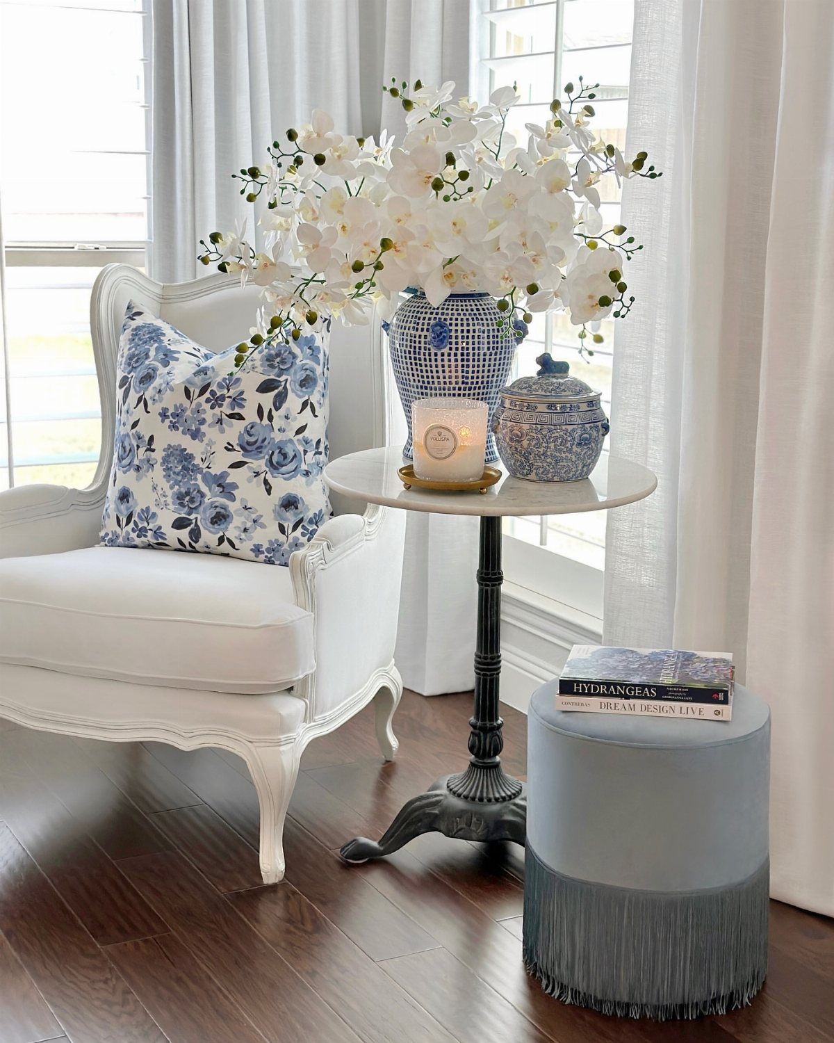 White ornate armchair and small round accent table with white flowers and candle.