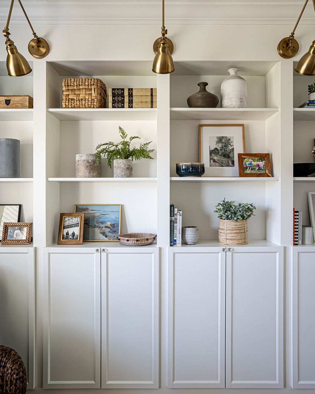 White built-in shelving unit with decorative objects and gold brass wall lamps above.