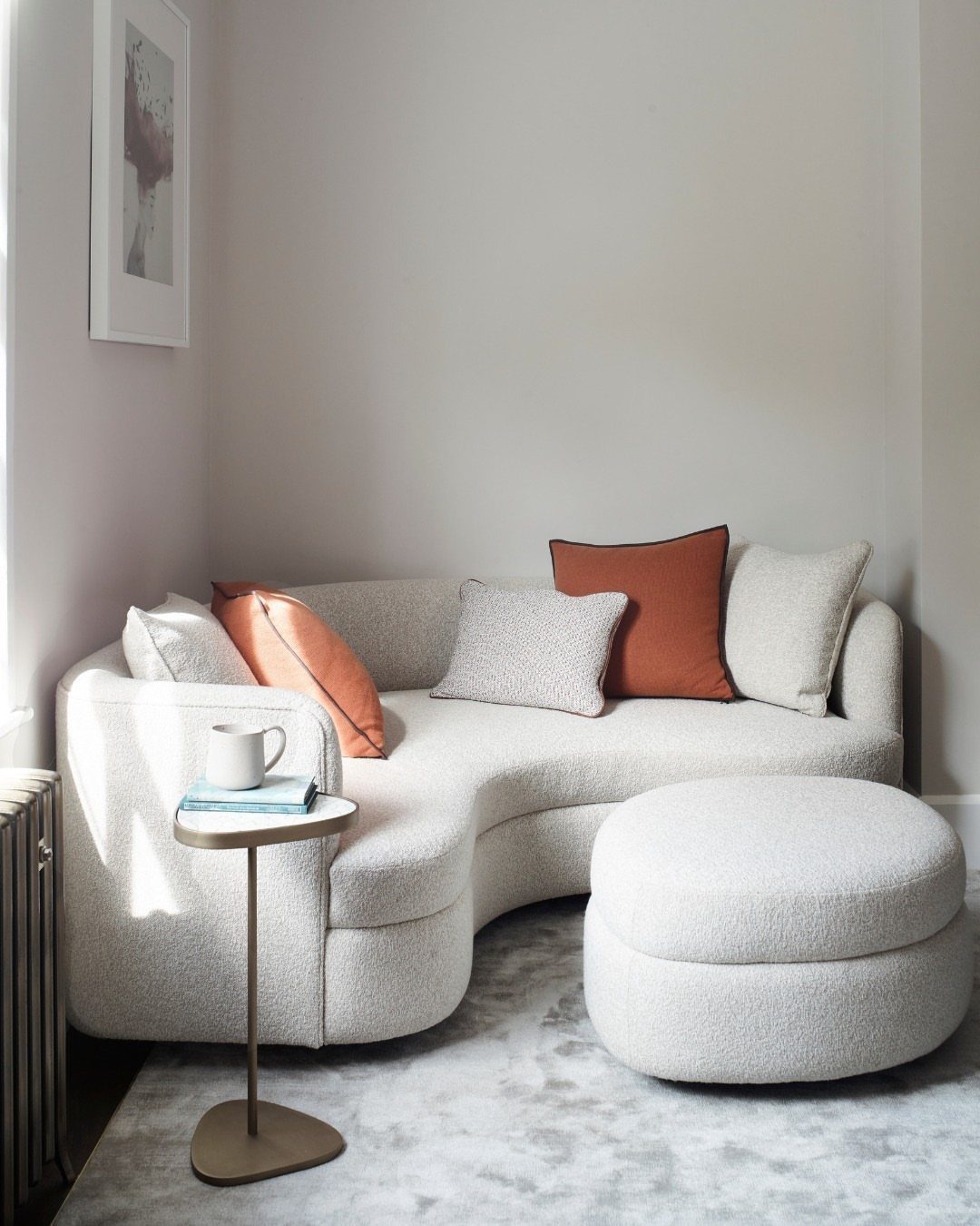 Curved white bouclé sofa and round ottoman in a minimalist living room setting.