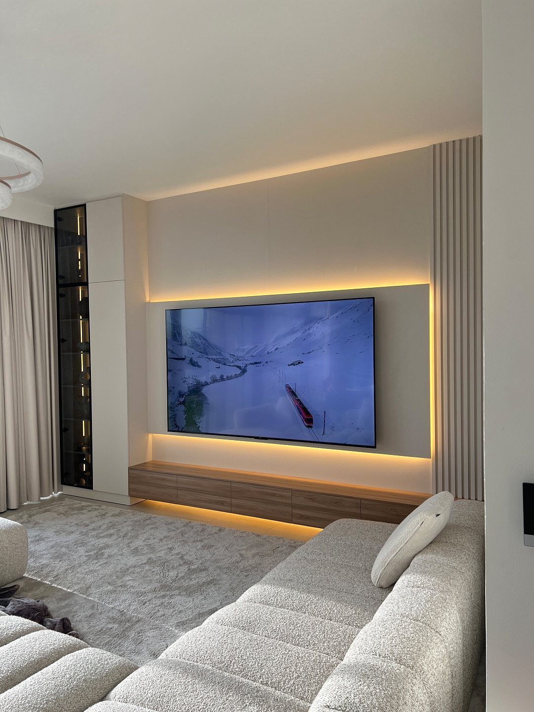 Modern living room with backlit TV, wooden console, and grey sectional sofa.