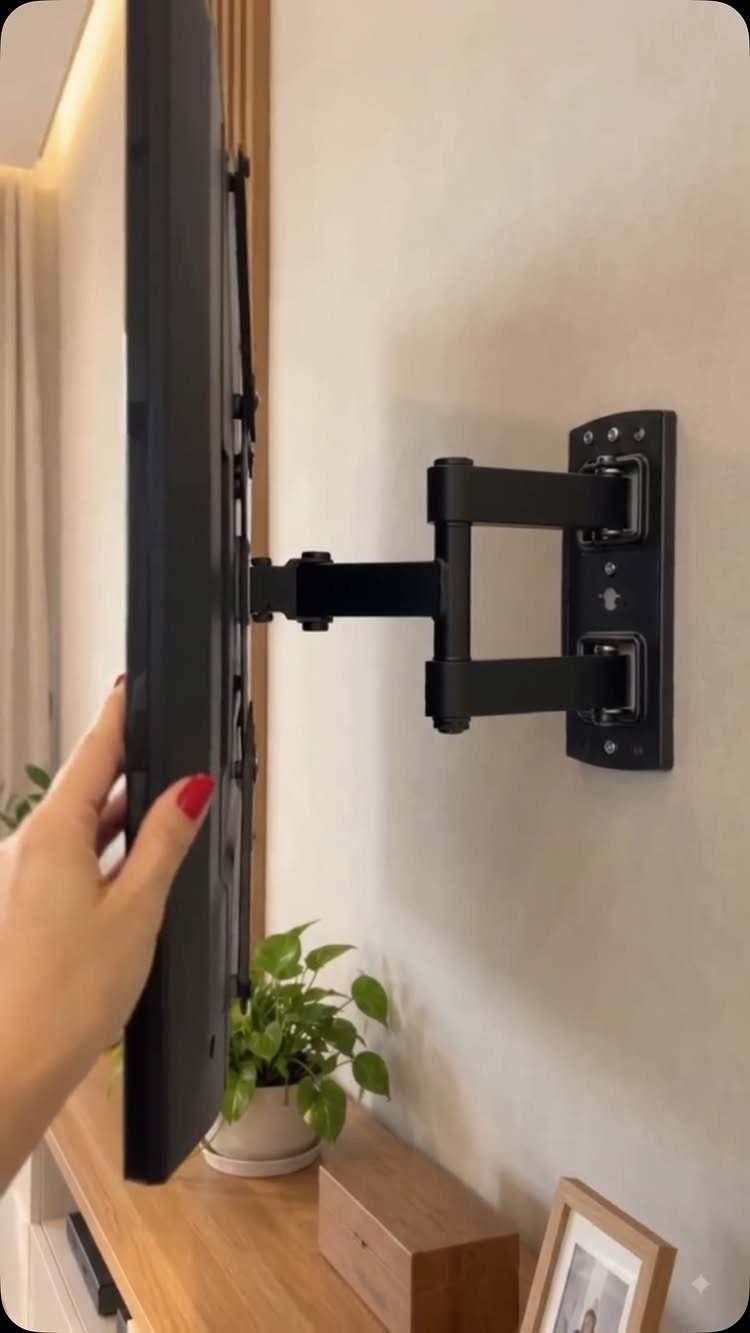 Black flat-screen TV attached to an articulated swivel wall mount being adjusted by hand.