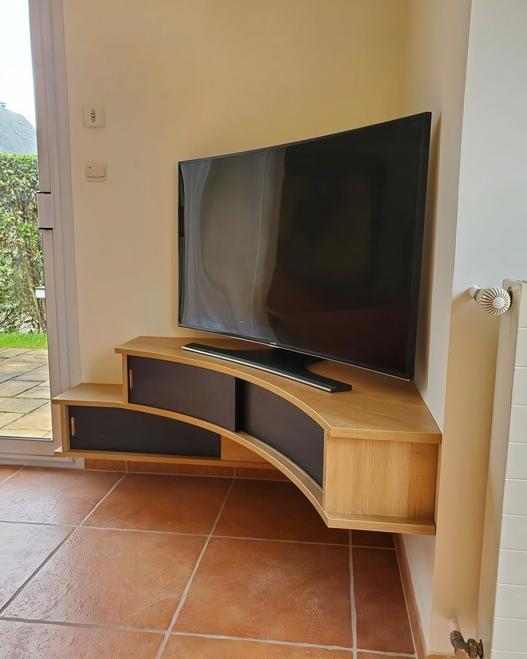 Flat-screen television on a curved wooden floating shelf against a beige wall.