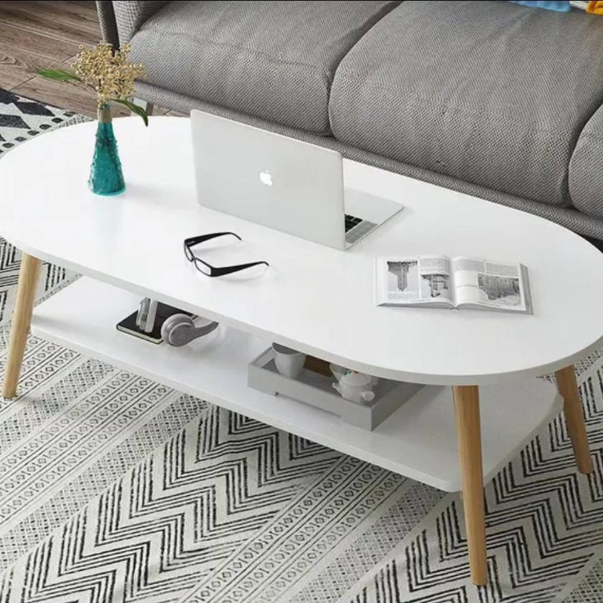 White oval coffee table with wooden legs and a laptop on a patterned rug.