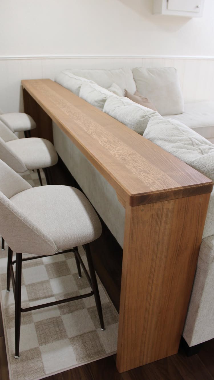 Wooden bar table with white stools placed behind a white fabric sofa.