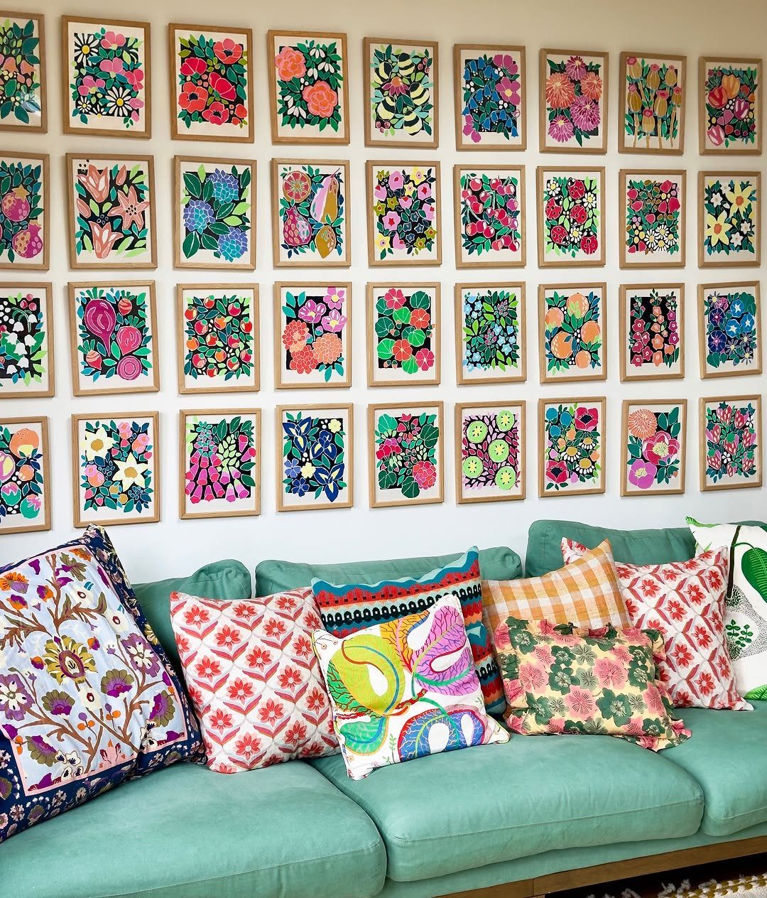 Teal sofa with colorful pillows in front of a grid gallery wall of floral art