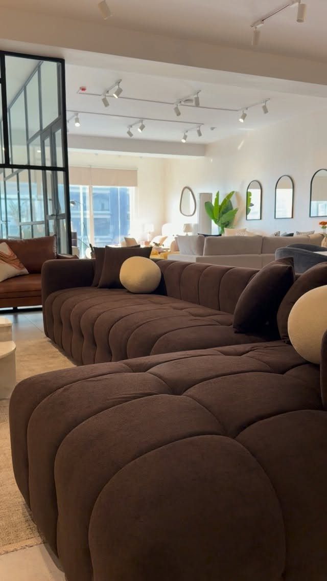 Brown tufted sectional sofa decorated with cream and brown throw pillows in showroom