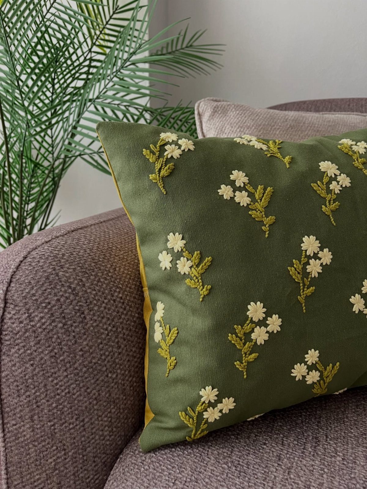 Green floral embroidered throw pillow on a brown textured fabric couch