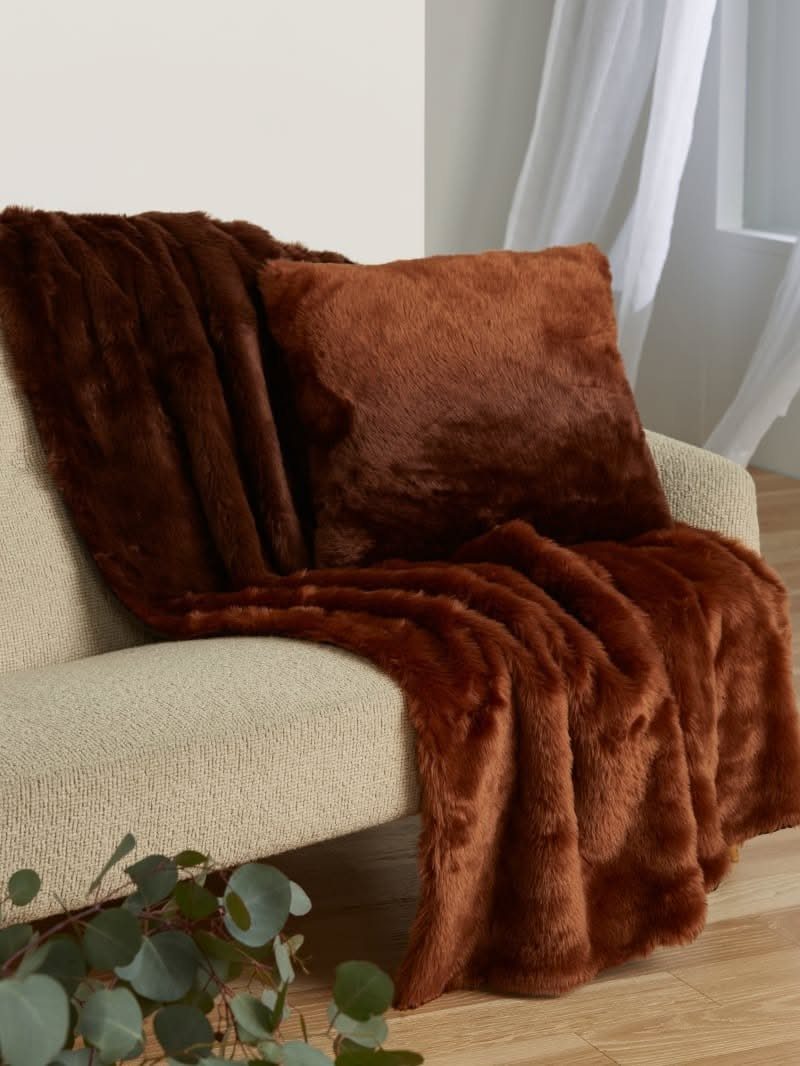 Brown faux fur throw pillow and matching blanket on a beige sofa.