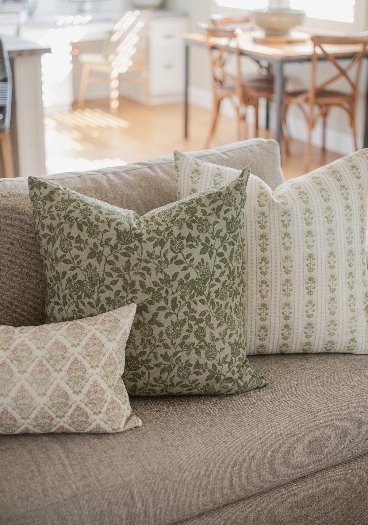 Sage green floral throw pillows on a brown couch in a bright room.