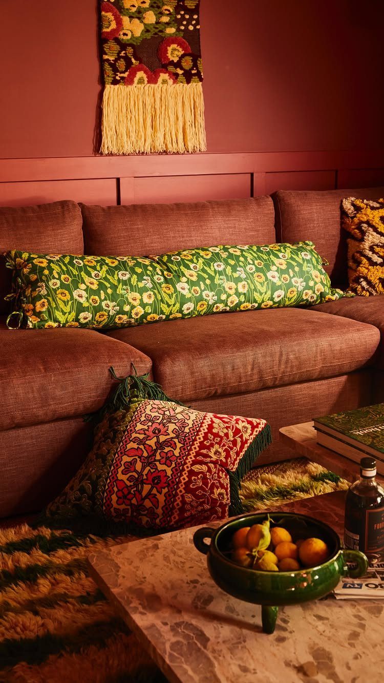 Brown couch with a long green floral bolster and red patterned throw pillows.
