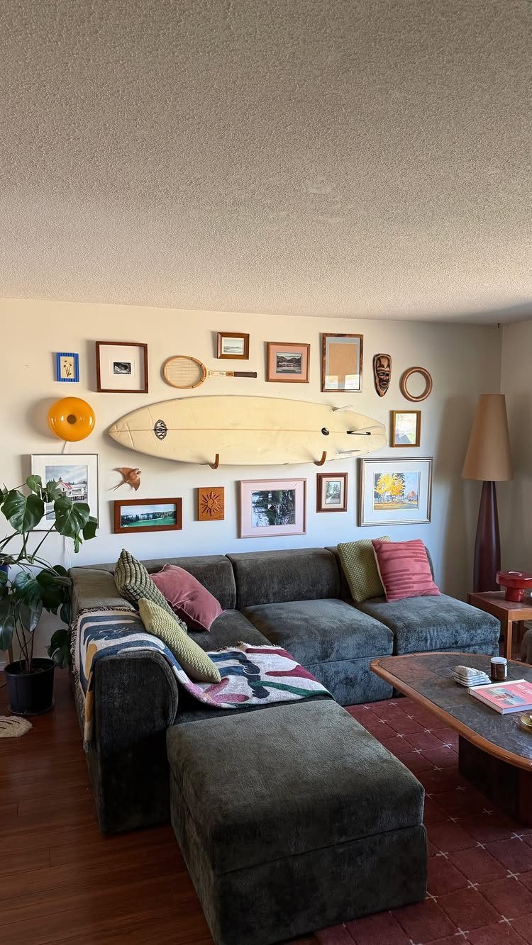 Grey sectional sofa with a surfboard and gallery wall decor behind it.