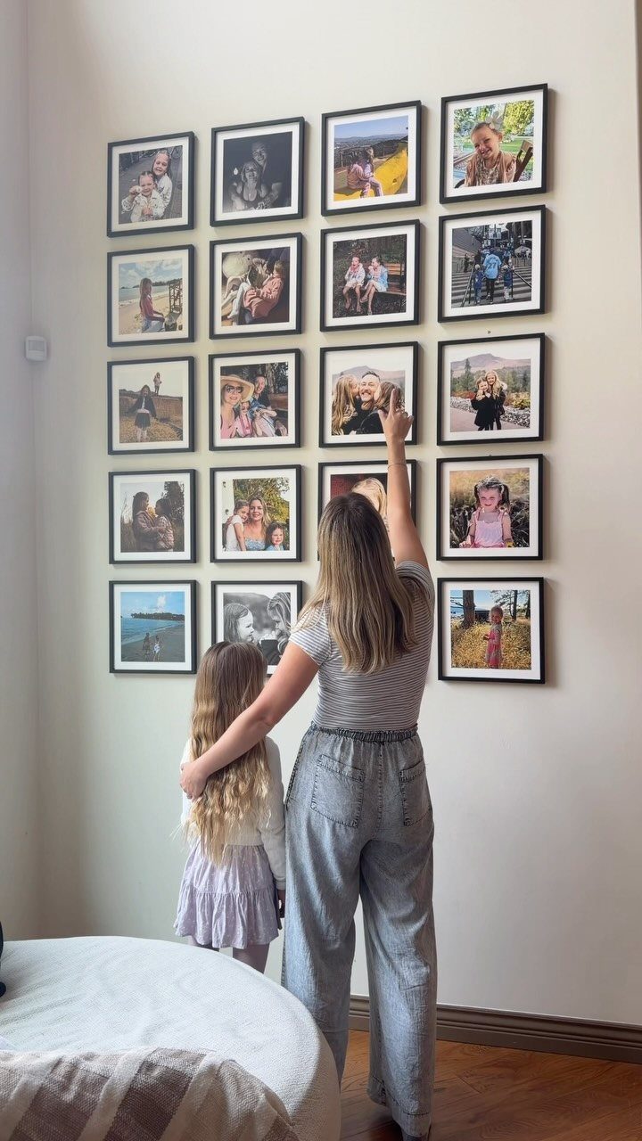 Woman and child arranging a grid of framed photos on a white wall