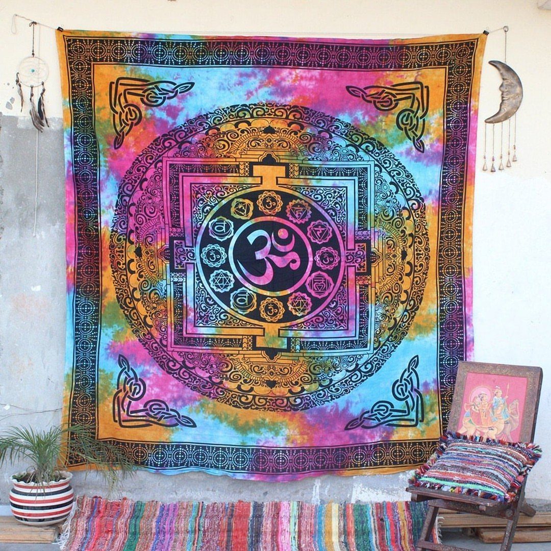 Colorful mandala tapestry with Om symbol hanging on a white wall above a rug.