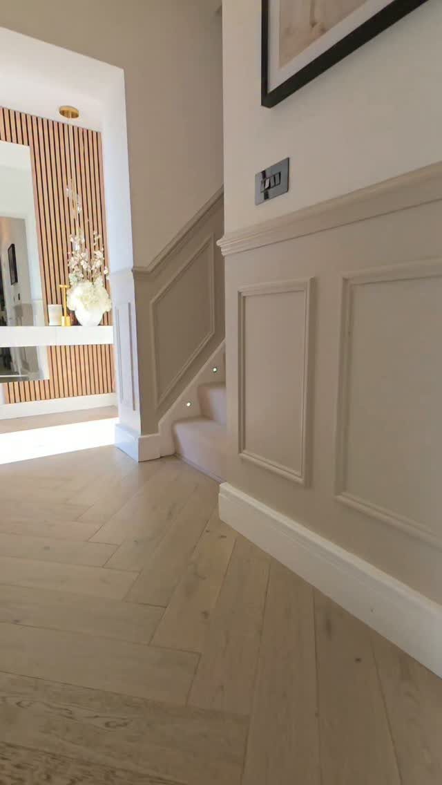 Grey wainscoting wall paneling in a hallway with light herringbone wood floors.