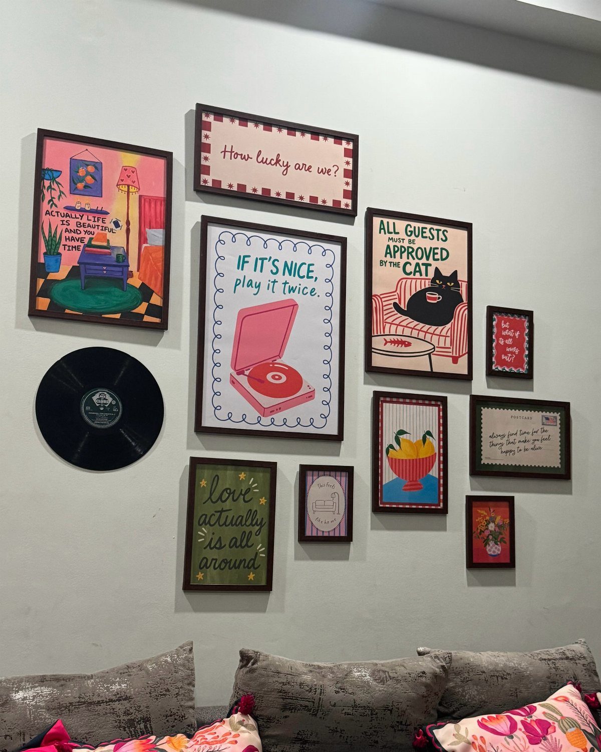 Assorted framed art and a vinyl record arranged on a wall above a sofa