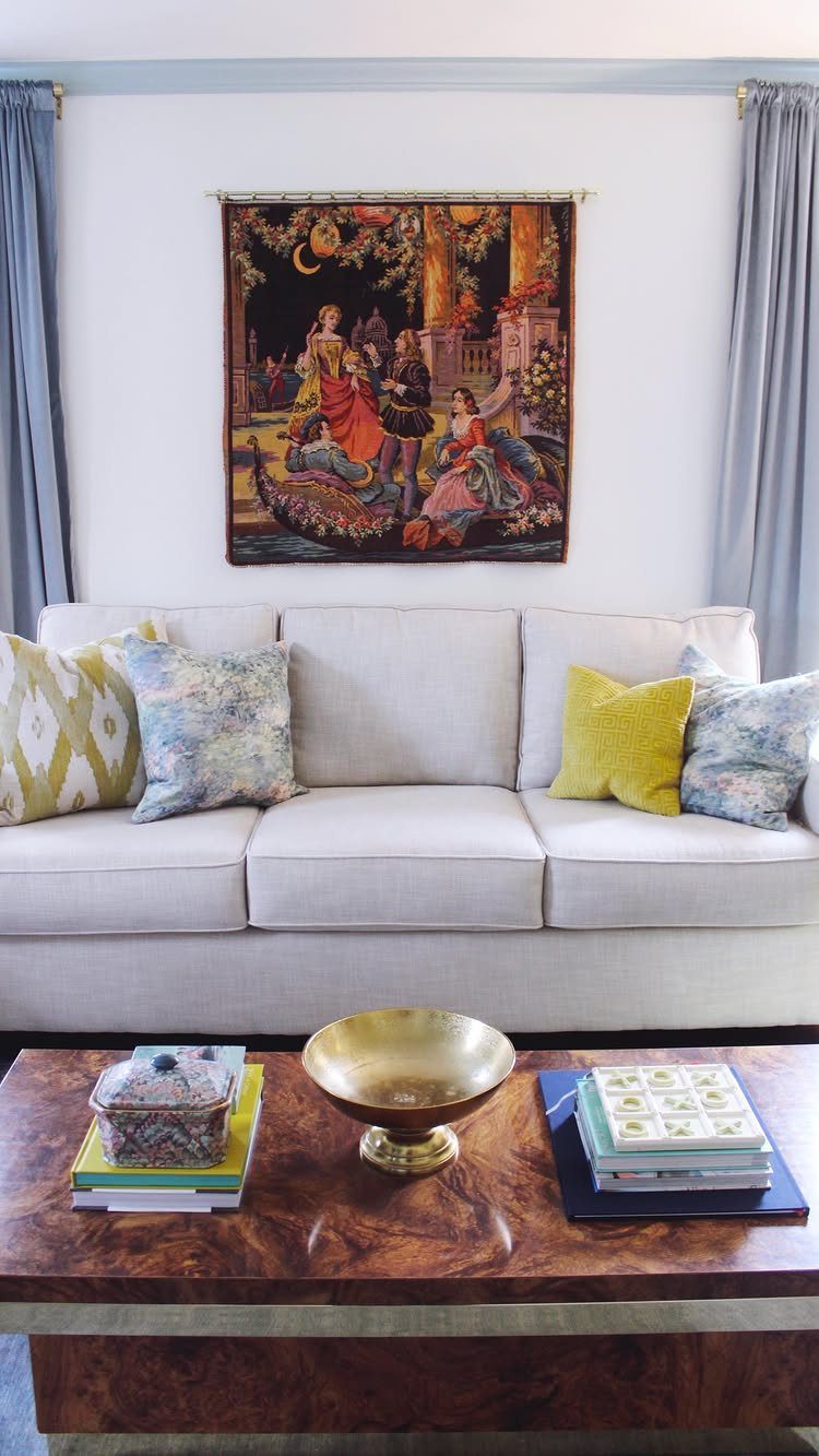 Ornate tapestry hanging on a white wall above a white sofa with pillows.