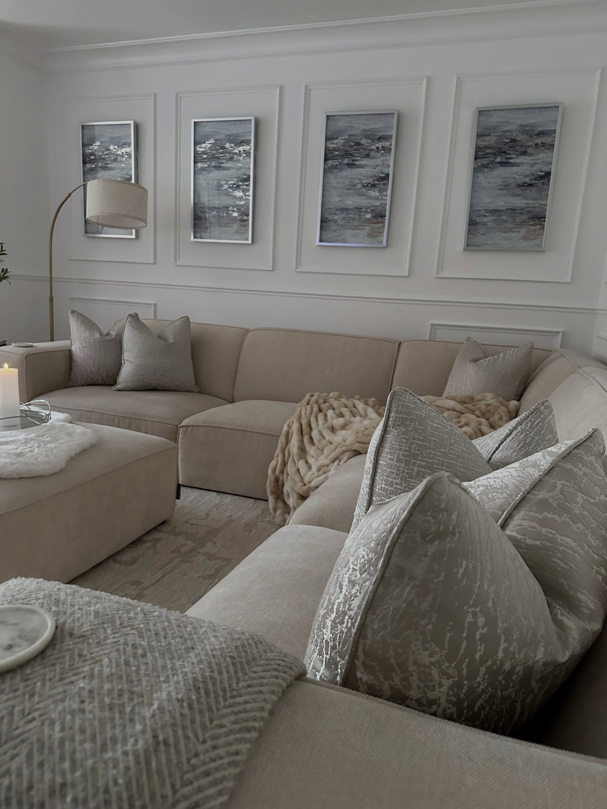 Beige sectional sofa with textured pillows and seascape paintings on a white wall
