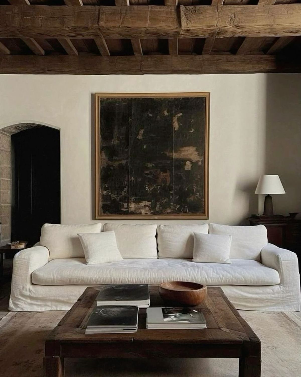 White fabric sofa in a rustic room with wooden beams and dark art.